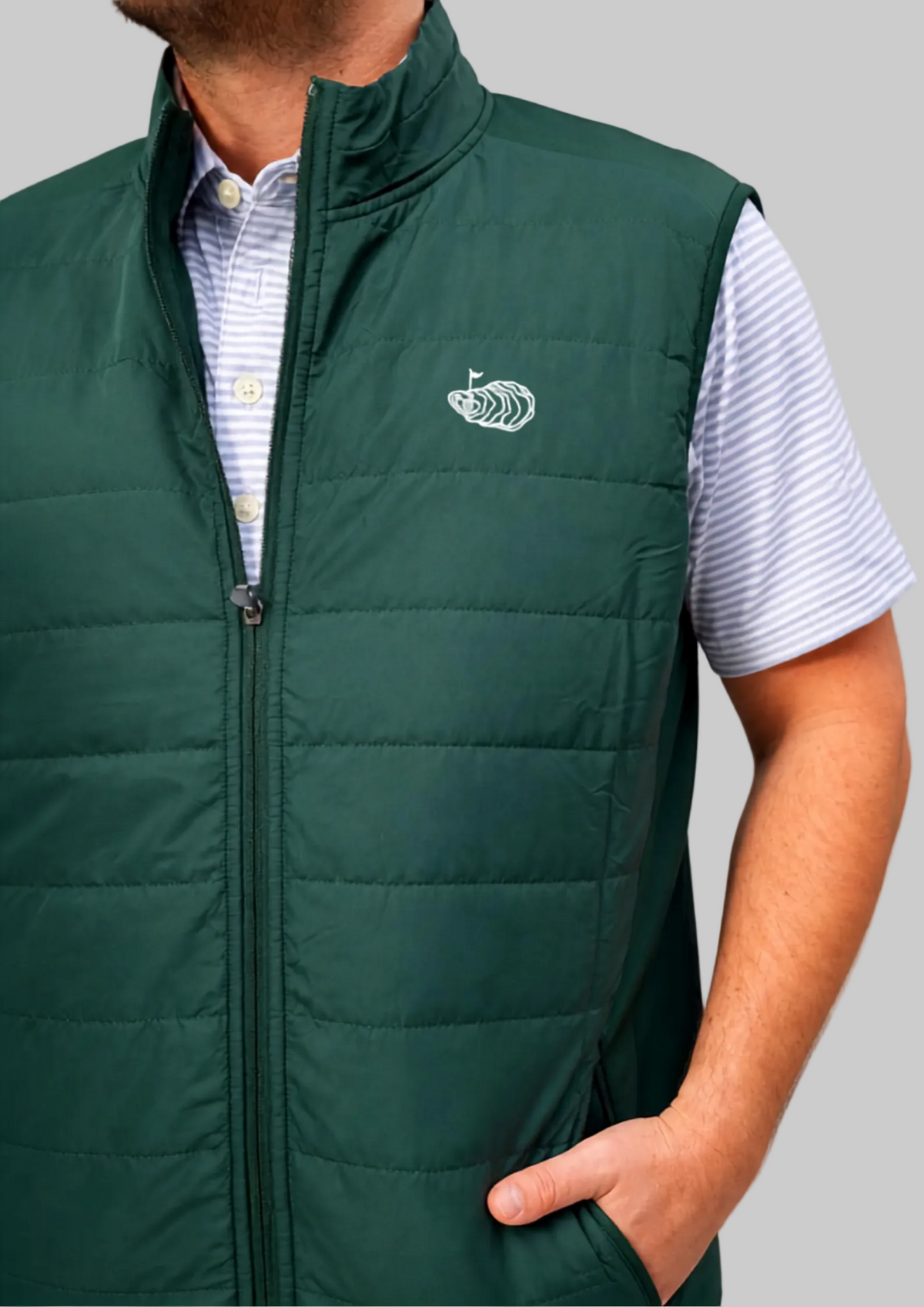 A dark green quilted zip-up vest worn by a model over a white and blue striped short-sleeve shirt, shown against a neutral gray background.